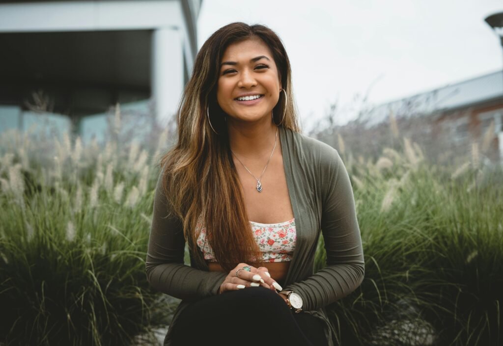 A woman smiling brightly while sitting outdoors, surrounded by lush greenery. Perfect for lifestyle and fashion themes.