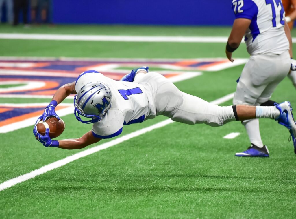 Football player making an incredible diving catch during a high-energy game in the stadium.